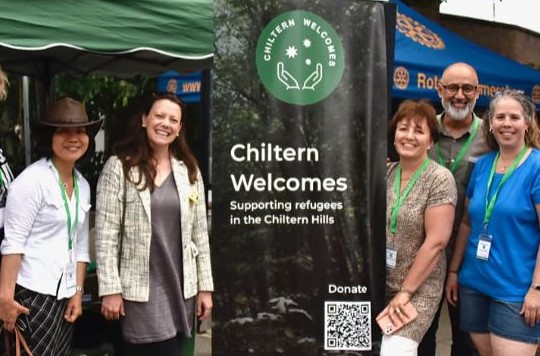 Photograph showing the Chiltern Welcomes stand at Refugee Week 2023 event with a few trustees and MP Sarah Green